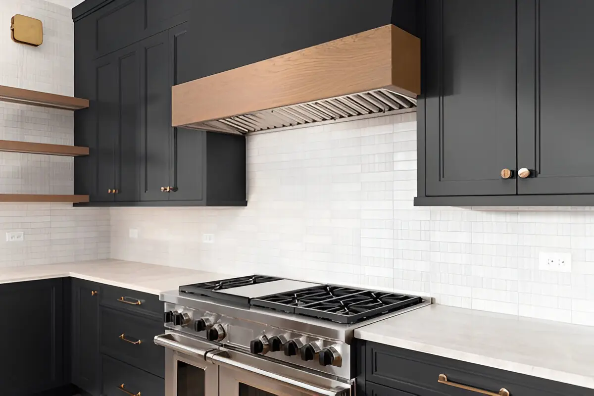 Modern kitchen with black cabinets, brass hardware, stainless steel gas range, and wood-trimmed range hood